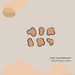 Peut inclure: Un logo pour une entreprise appelée "The Cutterist" spécialisée dans les découpeurs de design spéciaux. Le logo présente un groupe de six formes organiques brunes avec des contours noirs.