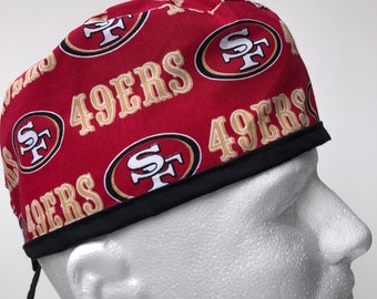 Puede incluir: Un gorro de quirófano rojo y dorado con el logotipo de los San Francisco 49ers y las palabras "49ers" repetidas en la tela.