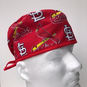 May include: Red and white surgical scrub hat with a St. Louis Cardinals baseball team print. The hat has a tie on the back and a white logo with the letters "STL" on the side.