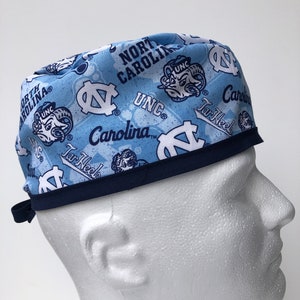 Puede incluir: Un gorro de quir&oacute;fano azul y blanco con estampado y ribete azul marino. El gorro presenta el logotipo de los UNC Tar Heels y las palabras "North Carolina" y "Tar Heels".