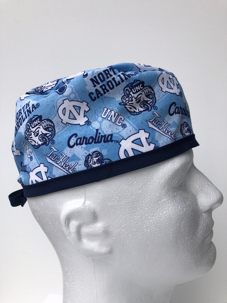 Puede incluir: Un gorro de quir&oacute;fano azul y blanco con estampado y ribete azul marino. El gorro presenta el logotipo de los UNC Tar Heels y las palabras "North Carolina" y "Tar Heels".