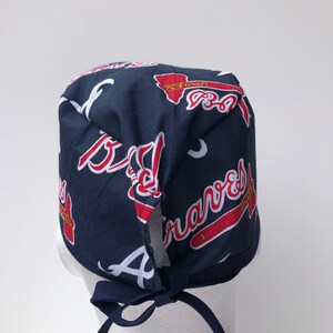 Peut inclure: Un bonnet de chirurgien bleu et rouge avec un motif r&eacute;p&eacute;t&eacute; du logo des Braves d'Atlanta. Le bonnet a une cravate &agrave; l'arri&egrave;re.