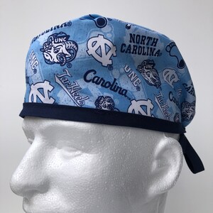 Puede incluir: Un gorro de quir&oacute;fano azul y blanco con estampado y ribete azul marino. El gorro presenta el logotipo de los Tar Heels de la Universidad de Carolina del Norte y el texto "North Carolina" y "Tar Heels".