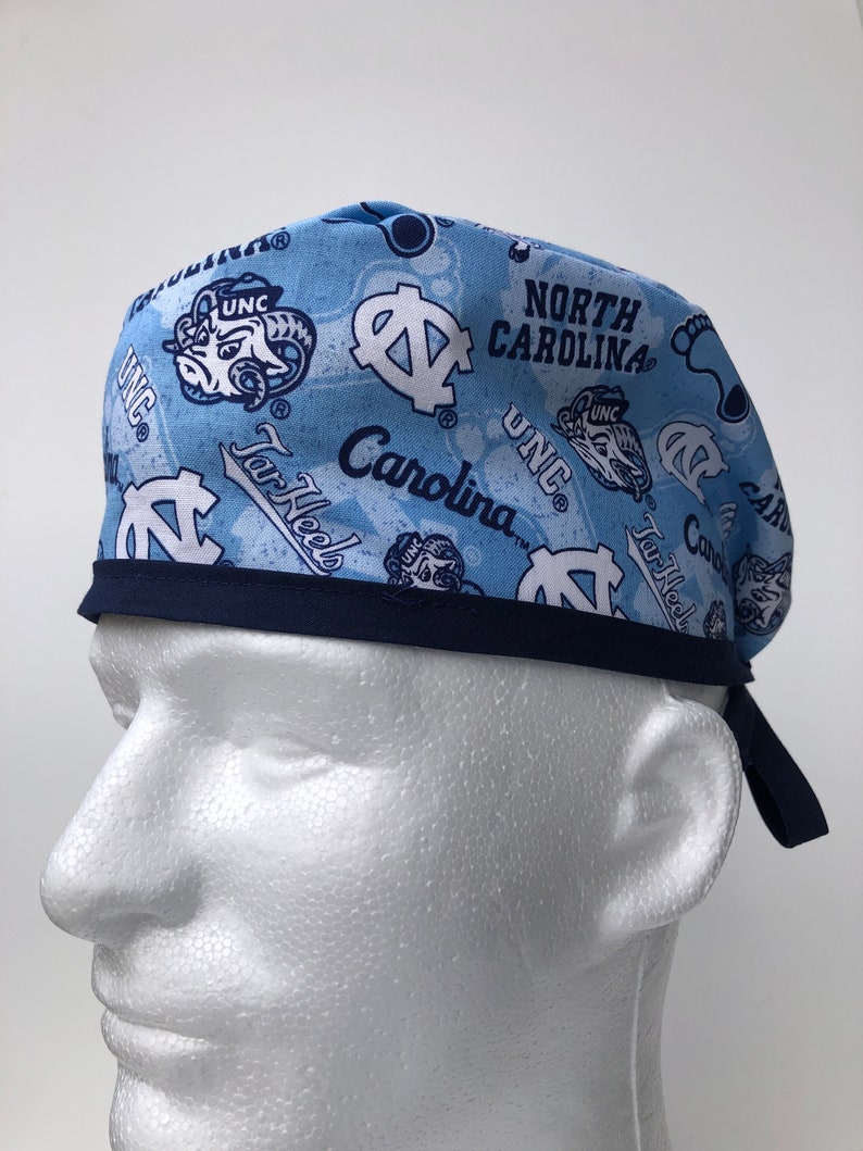 Puede incluir: Un gorro de quir&oacute;fano azul y blanco con estampado y ribete azul marino. El gorro presenta el logotipo de los Tar Heels de la Universidad de Carolina del Norte y el texto "North Carolina" y "Tar Heels".