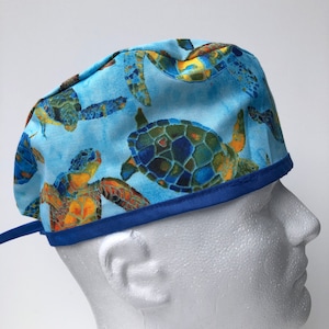 May include: A blue surgical scrub hat with a pattern of colorful sea turtles. The hat has a blue trim and a tie at the back.