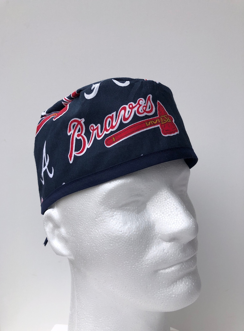 Peut inclure: Un bonnet de chirurgien bleu et rouge avec le logo des Braves d'Atlanta et le mot "Braves" en lettres blanches.