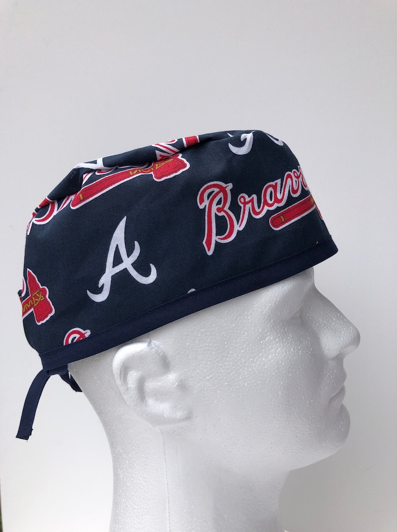 Peut inclure: Un bonnet de chirurgien bleu et rouge &agrave; motifs avec le texte "A Braves" imprim&eacute; dessus. Le bonnet a une cravate &agrave; l'arri&egrave;re.
