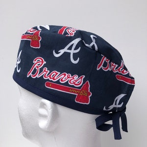 Peut inclure: Un bonnet de chirurgien bleu et rouge avec le logo des Atlanta Braves et les mots "Atlanta Braves" r&eacute;p&eacute;t&eacute;s sur le tissu.