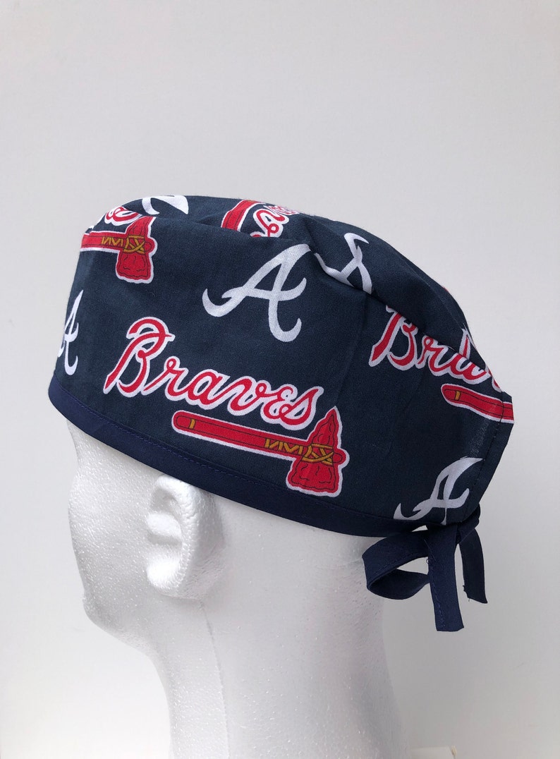 Peut inclure: Un bonnet de chirurgien bleu et rouge avec le logo des Atlanta Braves et les mots "Atlanta Braves" r&eacute;p&eacute;t&eacute;s sur le tissu.