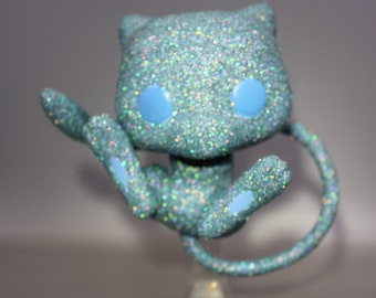 May include: A teal blue glitter figurine of a Pokemon character with blue eyes. The figurine is posed with its tail curled around its body.