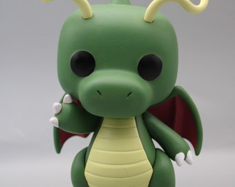 May include: A green dragon figurine with a light yellow belly and white claws. The dragon has large black eyes, red wings, and yellow curved horns. The figurine is a stylized, collectible item.