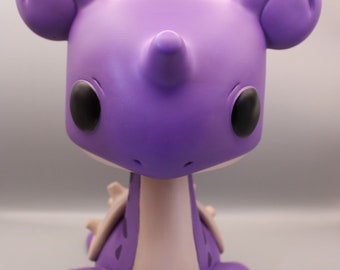 May include: Purple and pink ceramic figurine of a dragon with large ears, a horn, and black eyes.