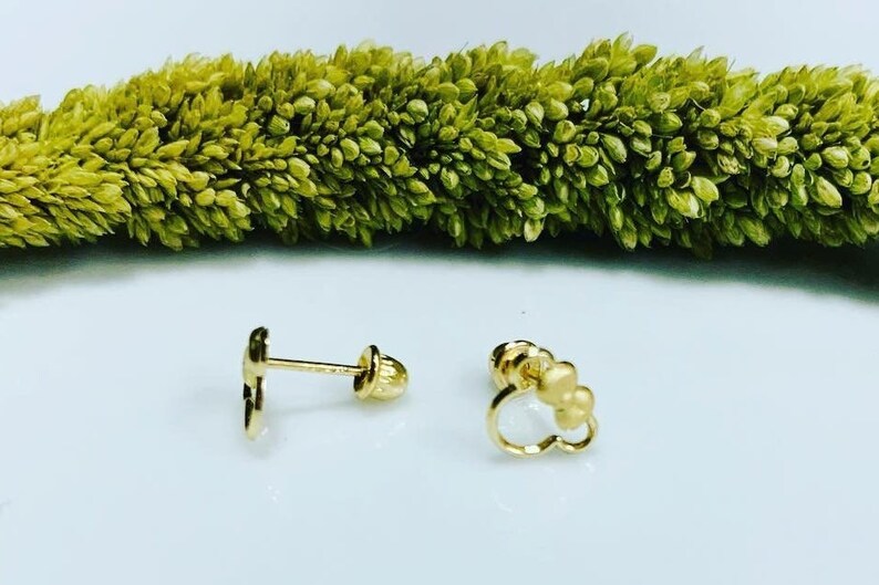 May include: A pair of gold-colored stud earrings. One earring features a heart shape with three small circles, while the other earring is a simple, solid heart shape.