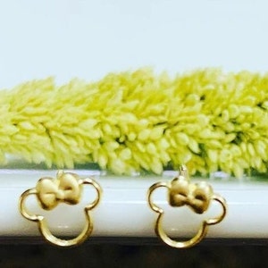 May include: A pair of gold-tone earrings with a bow and a Mickey Mouse silhouette design.