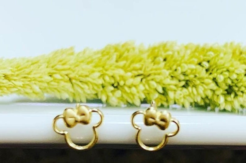 May include: A pair of gold-tone earrings with a bow and a Mickey Mouse silhouette design.