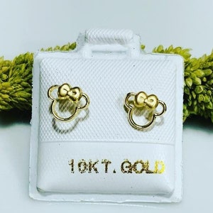 May include: A pair of gold-colored bow-shaped earrings on a white background. The earrings are in a small, white box with the text "10KT GOLD" printed on the bottom.
