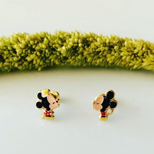 Puede incluir: Un par de pendientes de tono dorado con una imagen de dibujos animados de Mickey Mouse y Minnie Mouse bes&aacute;ndose. Los pendientes son peque&ntilde;os y delicados, perfectos para el uso diario.