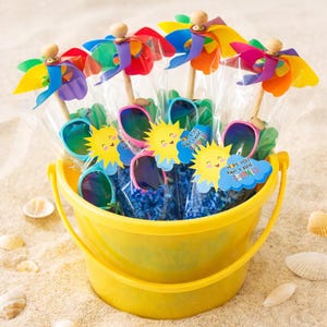 May include: A yellow plastic bucket filled with beach-themed party favors. The bucket contains colorful pinwheels, sunglasses, and tags with a smiling sun graphic and the text "Hope you have a great summer!" on a sandy background.