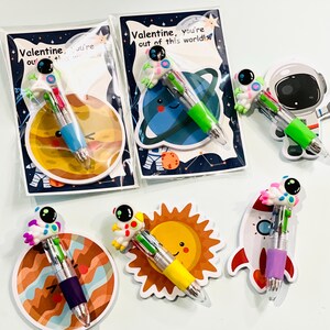 May include: Valentine's Day multi-color pens with astronaut toppers. Each pen has a different colored barrel and is paired with a space-themed card or cutout. The cards read "Valentine, you're out of this world!"
