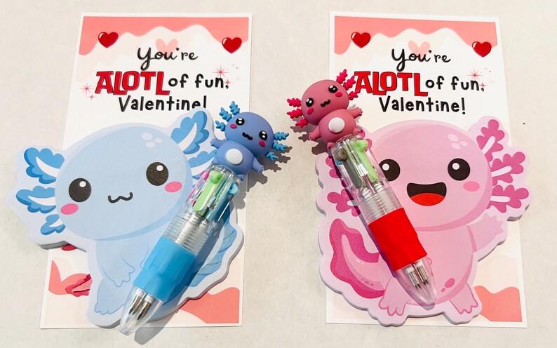 K&ouml;nnte beinhalten: Zwei Valentinstagskarten mit Axolotl-Illustrationen und mehrfarbigen Stiften. Auf den Karten steht "You're ALOTL of fun, Valentine!". Ein Axolotl ist blau, das andere rosa. Die Stifte haben mehrere Tintenfarben.