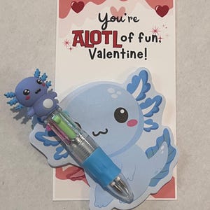 K&ouml;nnte beinhalten: Eine Valentinstagskarte mit einem hellblauen Axolotl-Design und einem mehrfarbigen Stift. Auf der Karte steht "You're ALOT of fun, Valentine!" in roter und schwarzer Schrift. Der Stift hat einen blauen Griff und einen transparenten Schaft.