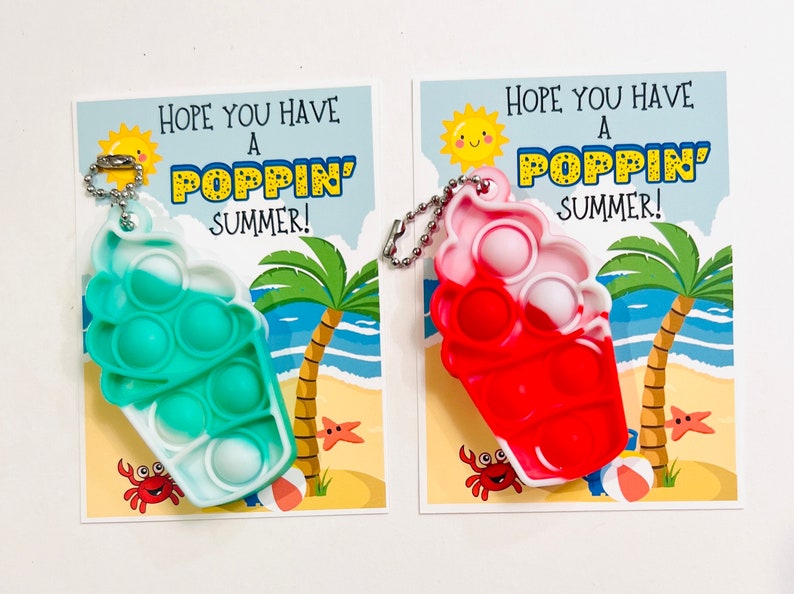 K&ouml;nnte beinhalten: Zwei bunte Pop-it-Schl&uuml;sselanh&auml;nger mit Sommerthema. Die Schl&uuml;sselanh&auml;nger sind in Form von Eiswaffeln gestaltet und haben ein wei&szlig;-blaues Pop-it und ein wei&szlig;-rotes Pop-it. Die Schl&uuml;sselanh&auml;nger sind an Karten mit dem Text "Ich hoffe, du hast einen tollen Sommer!" befestigt.