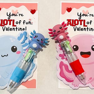 K&ouml;nnte beinhalten: Zwei Valentinstagskarten mit Axolotl-Stiften. Eine Karte zeigt einen blauen Axolotl und Stift, die andere einen rosa Axolotl und Stift. Jede Karte tr&auml;gt den Text "You're ALOT of fun, Valentine!" und Herzdekorationen.