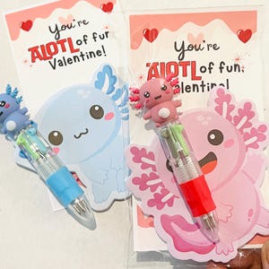 K&ouml;nnte beinhalten: Zwei Valentinstagskarten mit Stiften zum Thema Axolotl. Eine Karte zeigt einen blauen Axolotl und den Text "You're AIOTL of fur Valentine!" Die andere Karte hat einen rosa Axolotl und den Text "You're AIOTL of fun, Valentine!"