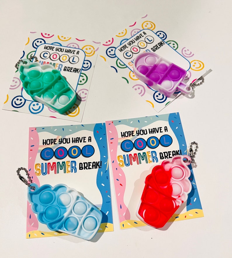K&ouml;nnte beinhalten: Vier bunte Pop-it-Fidget-Spielzeuge in Form von Eiswaffeln mit Schl&uuml;sselanh&auml;ngern. Jedes Spielzeug hat eine andere Farbkombination und ist mit einer Karte versehen, auf der steht: "Ich hoffe, du hast coole Sommerferien!"