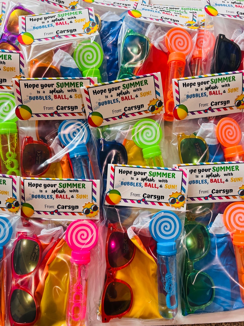 May include: A set of colorful summer party favor bags with a variety of items, including sunglasses, bubble wands, and small inflatable balls. Each bag has a tag that says "Hope your summer is a splash with bubbles, ball, & sun!" and is signed "From: Carsyn".
