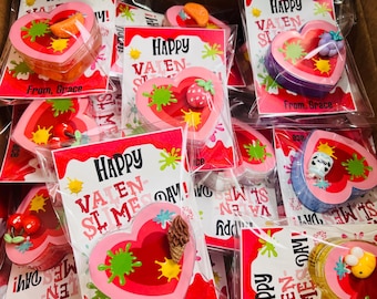 May include: A collection of Valentine's Day slime favors in heart-shaped containers. Each container has a different colorful slime and a cute topper. The containers are decorated with pink and red paint splatters and the text "Happy Valentine Slime Day!"
