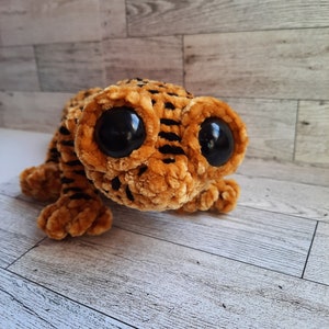 May include: A brown and black plush toy gecko with large, black googly eyes. The gecko is made of a soft, fuzzy material.