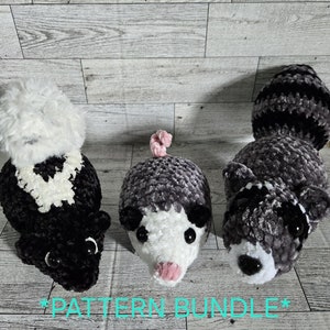 Puede incluir: Tres animales de peluche tejidos a crochet: una mofeta blanco y negro, una zarigüeya gris y blanca y un mapache gris. Los animales están todos sentados sobre una superficie de madera. *PATTERN BUNDLE*