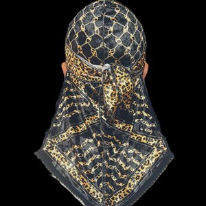 Puede incluir: Un durag negro y dorado con un patrón de cadena en la parte superior y un diseño de estampado de leopardo en la solapa. El durag tiene una cremallera y un cierre de lazo. Los bordes están adornados con encaje negro.