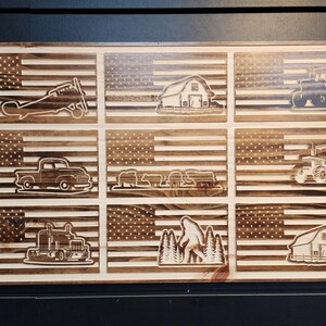 May include: A wooden sign with nine different images of American flags with various designs, including a barn, a tractor, a truck, a plane, a bigfoot, and a semi-truck.