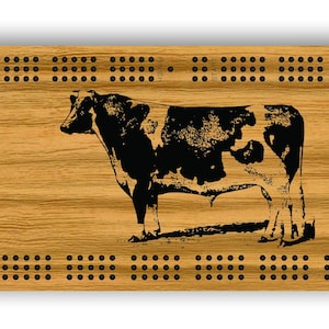 Könnte beinhalten: Ein Cribbage-Brett aus Holz mit einem Schwarz-Weiß-Kuh-Design. Das Brett ist rechteckig mit abgerundeten Ecken und einem schwarzen Rand.