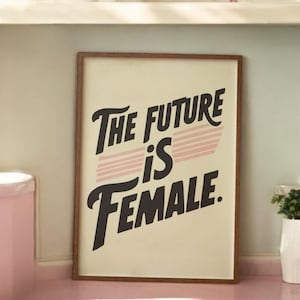 Puede incluir: Una impresión enmarcada con un fondo crema y un gráfico en blanco y negro que dice "The future is female." El gráfico tiene rayas rosas detrás del texto.