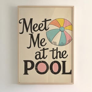 May include: Framed poster with the text "Meet Me at the Pool" in black script and block letters. A colorful beach ball illustration is next to the text. The poster has a vintage, retro style with a light beige background.