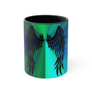 Pode incluir: Uma caneca de café preta com um fundo degradê verde e azul e uma silhueta preta de asas de anjo.