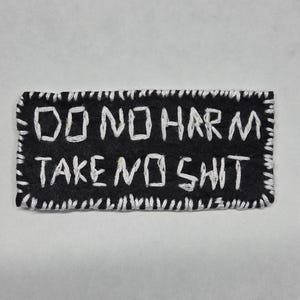 Peut inclure: Écusson rectangulaire noir avec texte blanc cousu : "DO NO HARM TAKE NO SHIT". L'écusson a une bordure blanche cousue.