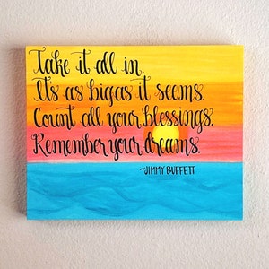 May include: A yellow, orange, and pink sunset painted on a wooden sign with the quote "Take it all in. It's as big as it seems. Count all your blessings. Remember your dreams." by Jimmy Buffett.