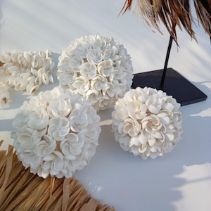 Peut inclure: Trois sphères décoratives blanches faites de petites coquillages blancs. Les sphères sont disposées sur une surface blanche.
