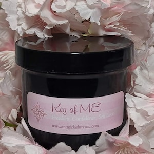 May include: A black jar with a pink label that reads "Key of ME Freedom, Confidence, Self Love" and "www.magicalmystic.com". The jar is surrounded by pink flowers.