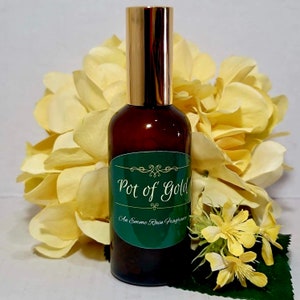 Pode incluir: Uma garrafa de vidro marrom com uma tampa dourada e um rótulo verde que diz "Pot of Gold An Emme Rain Fragrance".