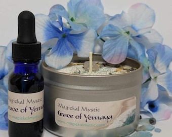 May include: A silver candle tin with a white candle and blue and green crystals. The candle is labelled "Magickal Mystic Grace of Yemaya" and has a website address. A blue glass bottle with a black dropper cap is next to the candle tin. The candle and bottle are surrounded by blue and green stones.