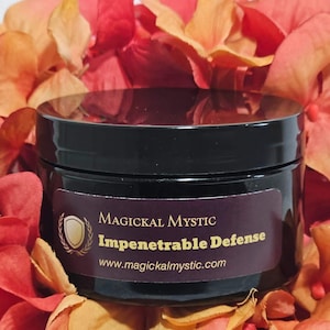 May include: A black jar with a gold label that reads "Magickal Mystic Impenetrable Defense www.magickalmystic.com". The jar is surrounded by orange and red flower petals.