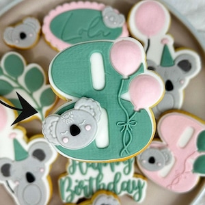 Könnte beinhalten: Ein Teller mit dekorierten Zuckerkeksen mit einer grünen Zahl Acht, einem Koalabären und den Worten "Happy Birthday". Die Kekse sind mit rosa und weißem Zuckerguss verziert.