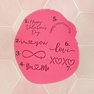 Könnte beinhalten: Ein rosa, unregelmäßig geformtes Objekt mit verschiedenen Texten zum Valentinstag. Der Text enthält "Happy Valentine's Day", "I love you", "You & Me", "love" und "XOXO". Der Hintergrund ist ein hellrosa sechseckiges Kachelmuster.