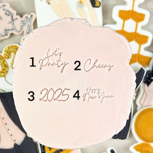 May include: A pink and white cake decorated with gold and black fondant. The cake is decorated with the numbers 2025, the words "Let's Party", "Cheers", and "Happy New Year".