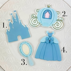 May include: Four blue and white sugar cookies decorated with royal blue icing. The cookies are shaped like a castle, a carriage, a dress, and a mirror. The cookies are numbered 1 through 4.